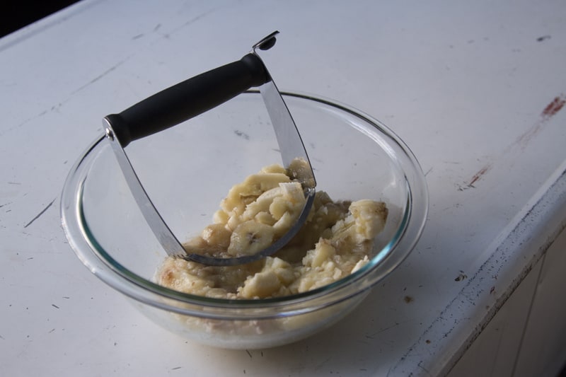 Mashed bananas in a glass bowl with a pastry blender. 