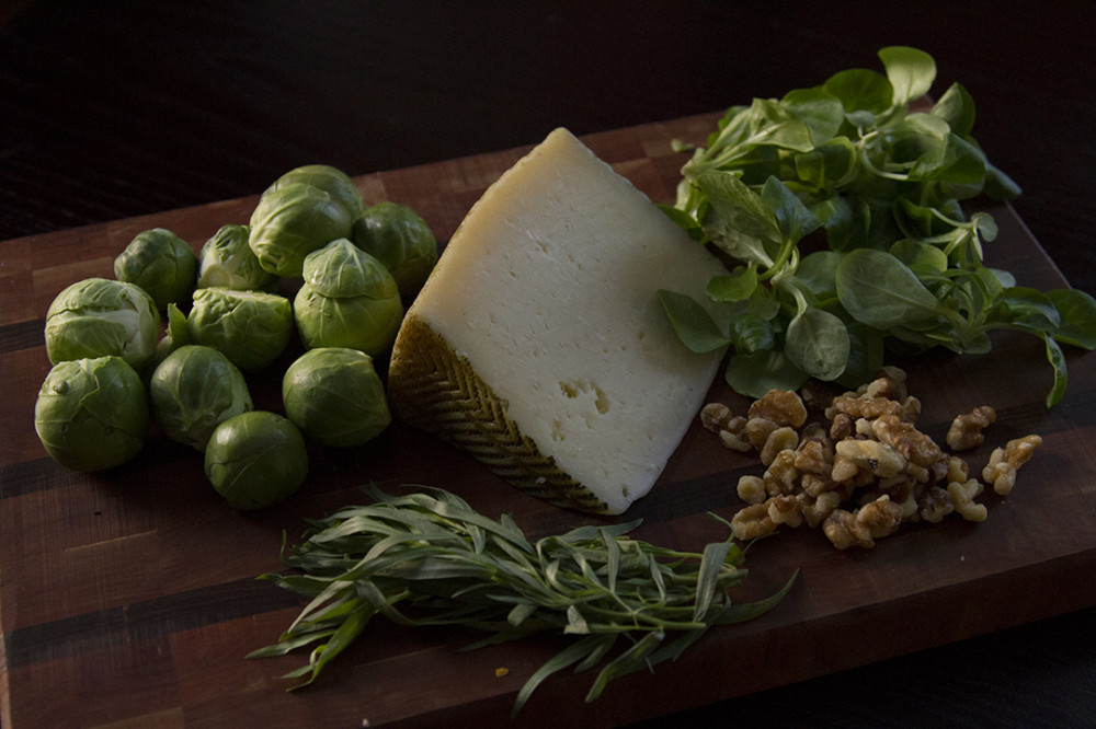 Brussels sprouts, Iberico cheese, mache, tarragon, and walnuts on a wooden cutting board. 