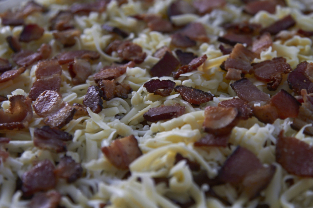 Grated cheese and bacon on top of  a pizza crust, ready for baking.