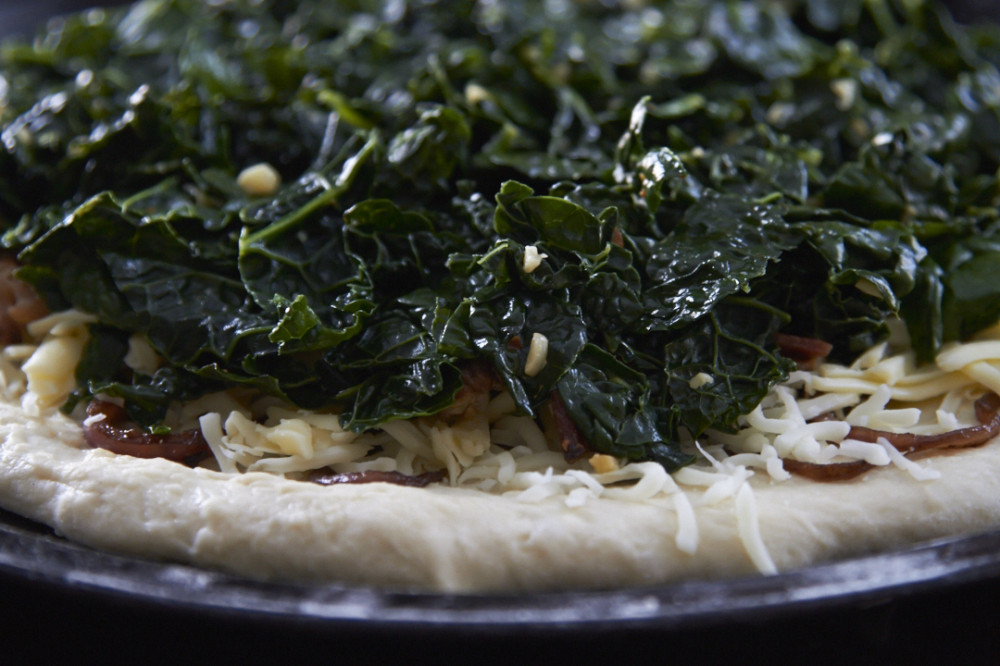 Kale, bacon and cheese on top of  a pizza crust ready for baking.
