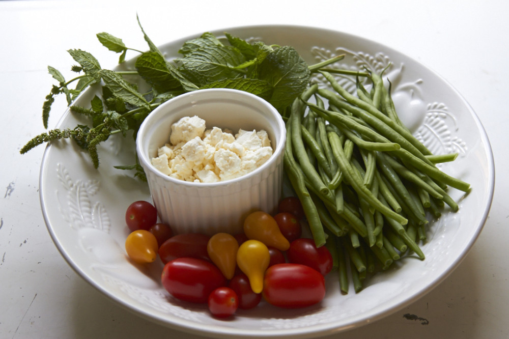 Fresh mint, green beans, tomatoes, and feta chees in a large white bowl.