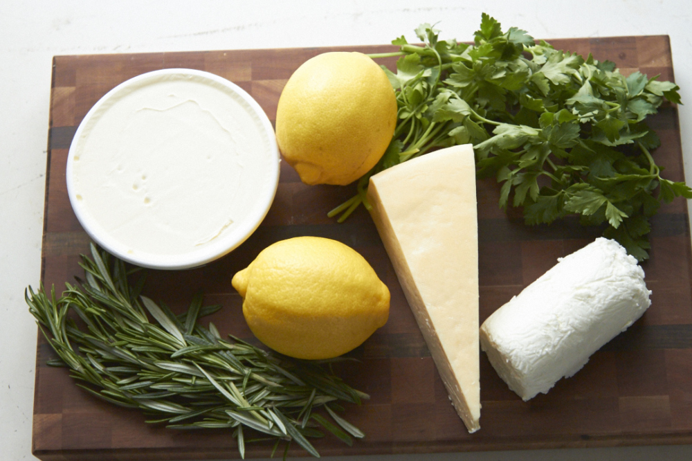 Mascarpone, goat cheese, parmesan and fresh herbs on a wooden cutting board. 
