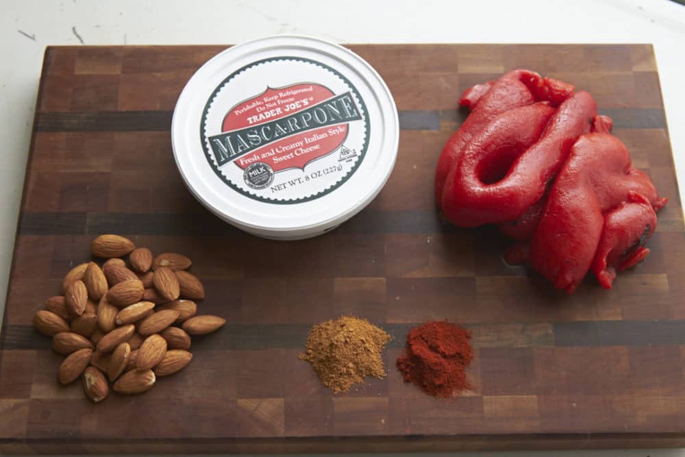 Mascarpone cheese, roasted red peppers, almonds and spices on a wooden cutting board. 