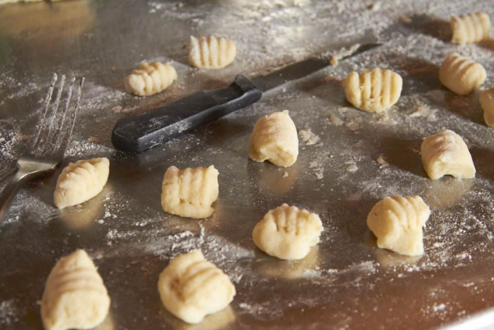 Gnocchi dumplings imprinted with fork tines on a counter top.
