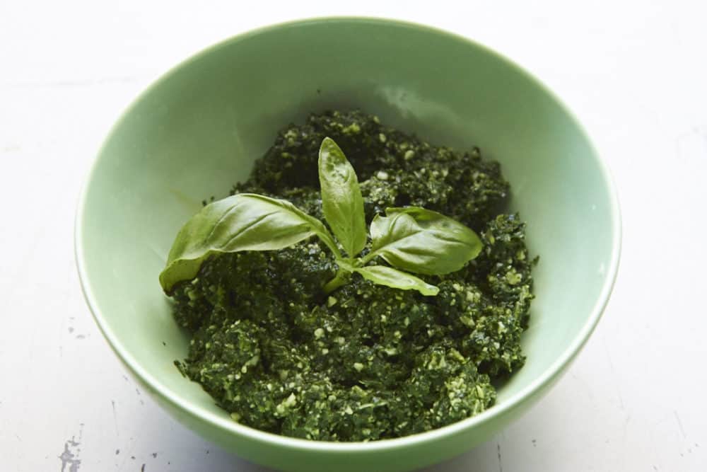 Kale pesto in a green bowl garnished with fresh basil.