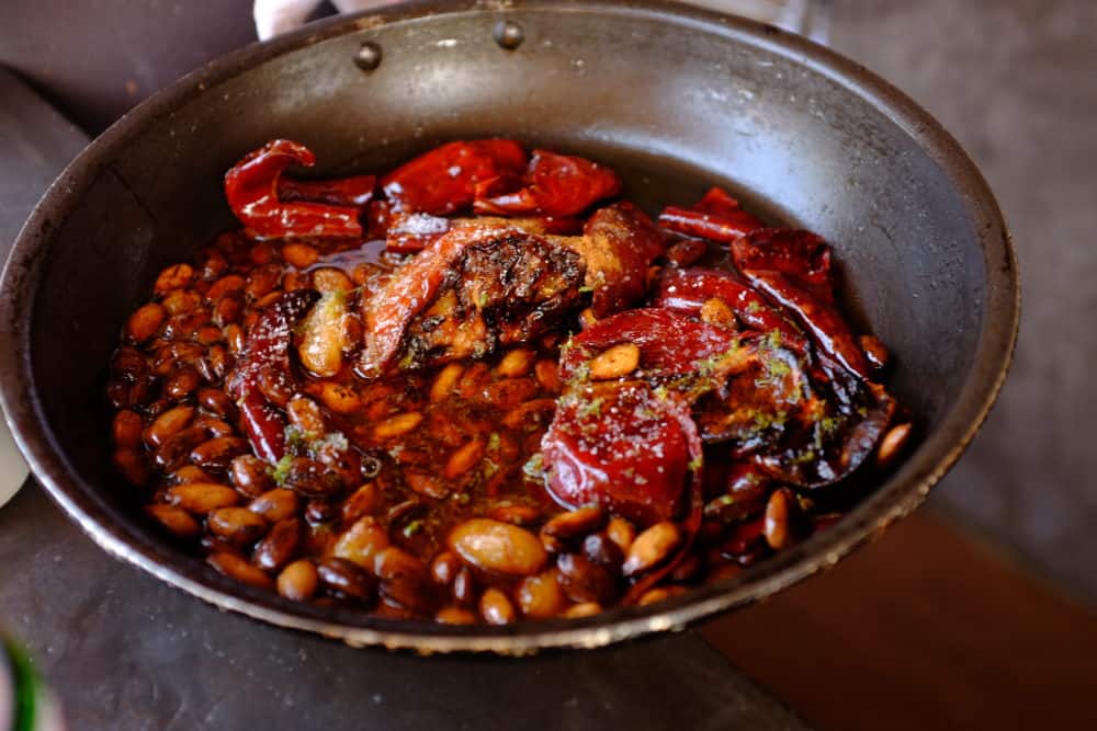 A skillet filled with almonds, chiles, tomatoes, garlic, honey and spices.
