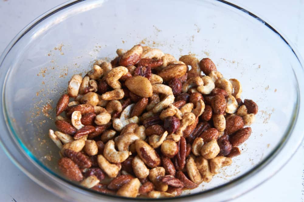 Mixed nuts coated with egg whites and spices in a glass bowl.