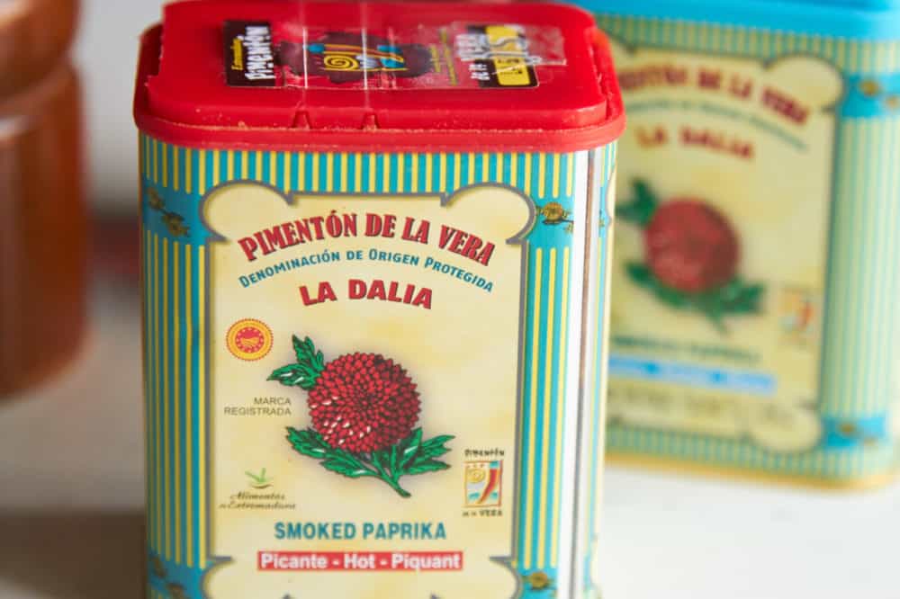 A can of hot smoked Spanish paprika with a red top, another can of sweet smoked paprika with a blue top in background.