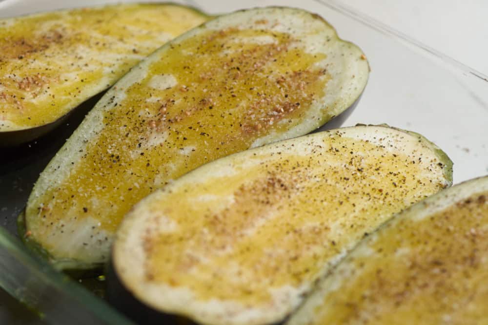 Raw eggplant halves in a baking dish, coated with olive oil, salt and pepper. 
