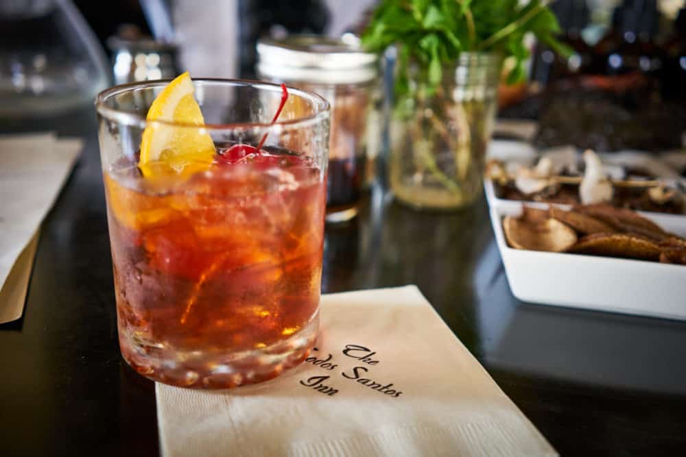 An Old Fashioned cocktail sits on a bar on a napkin that reads, "The Todos Santos Inn". Other garnishes for drinks are in the background. Photo by Brian Cummings. 