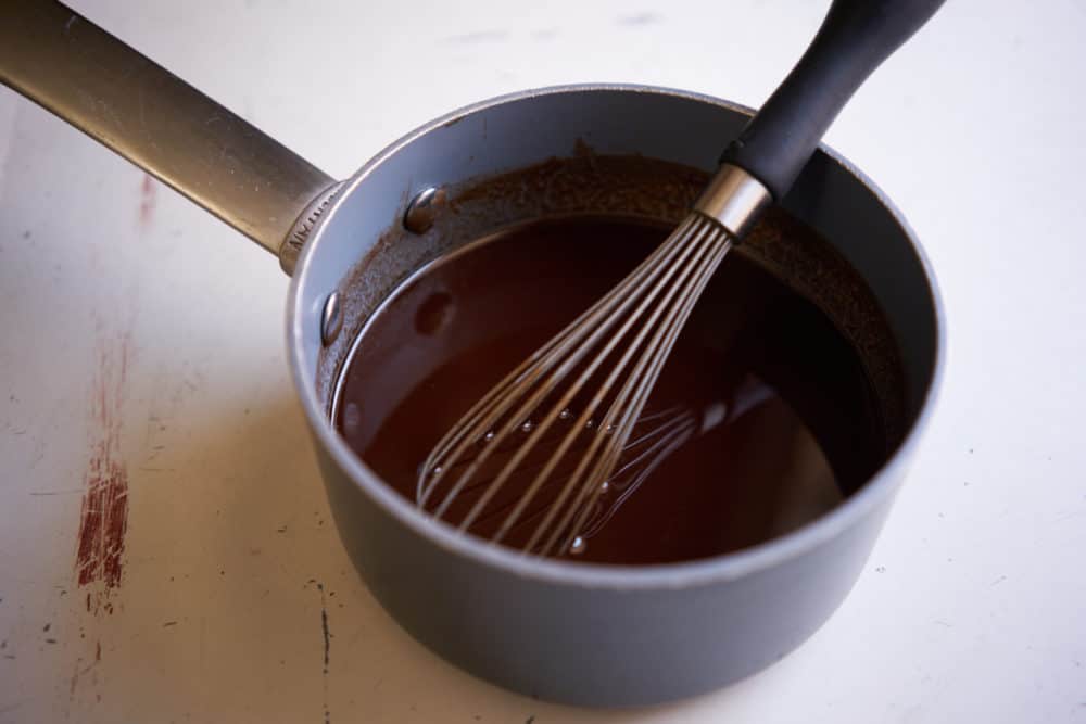 A whisk in a small sauce pan containing melted chocolate.