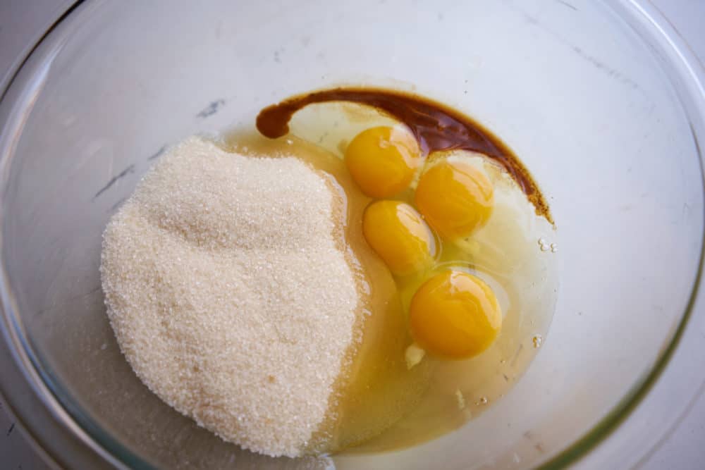 A clear glass bowl with sugar, eggs, and vanilla.