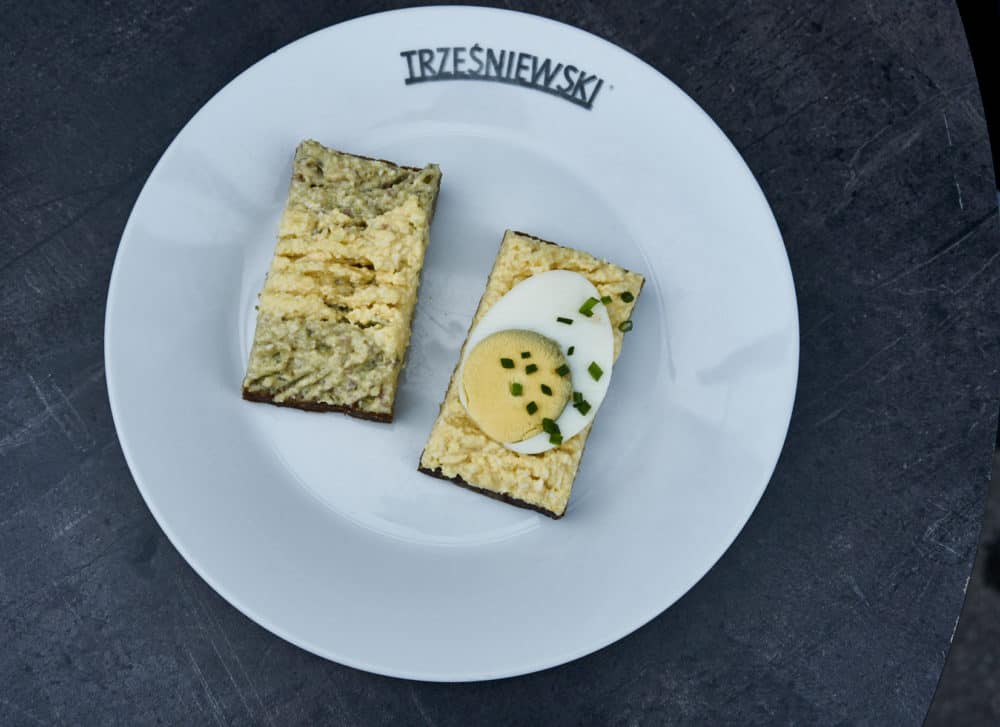 A white plate with two Trzesniewski open-faced sandwiches with hard boiled egg and egg salad.