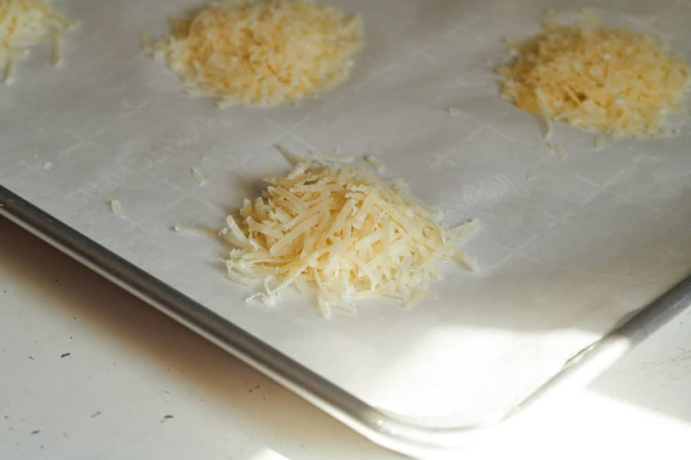 Stacks of shredded parmigiano reggiano on parchment paper arranged on a baking sheet.