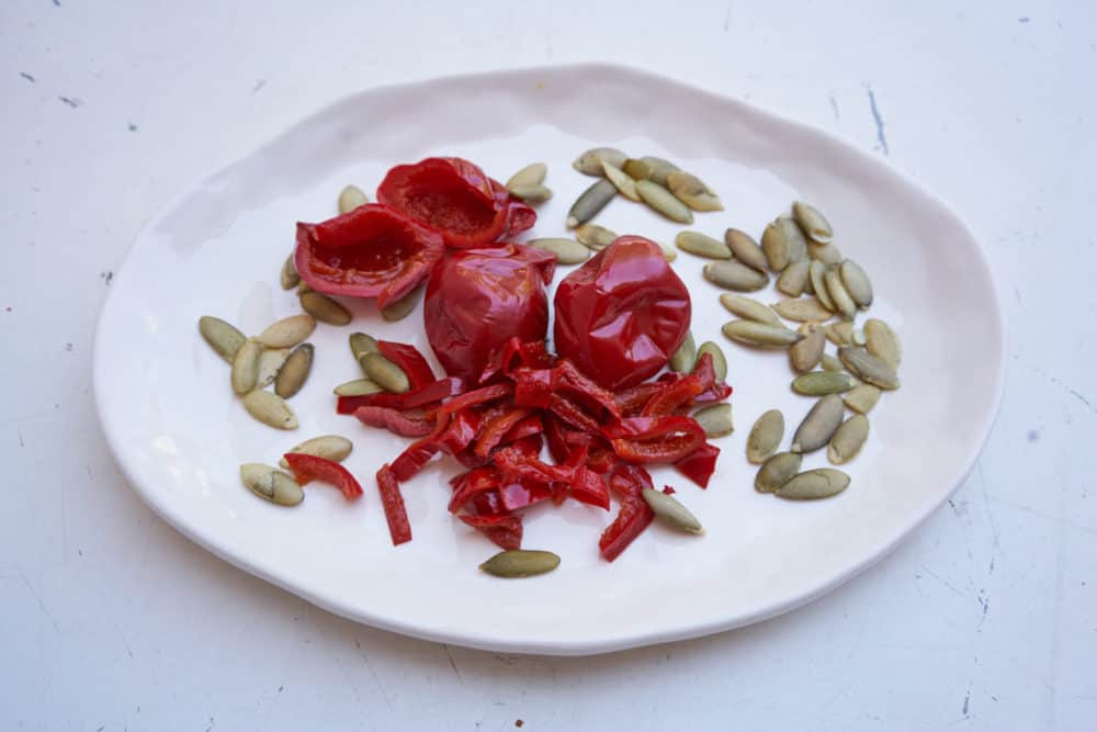Pepitas (pumpkin seeds) and cherry peppers on a white plate.
