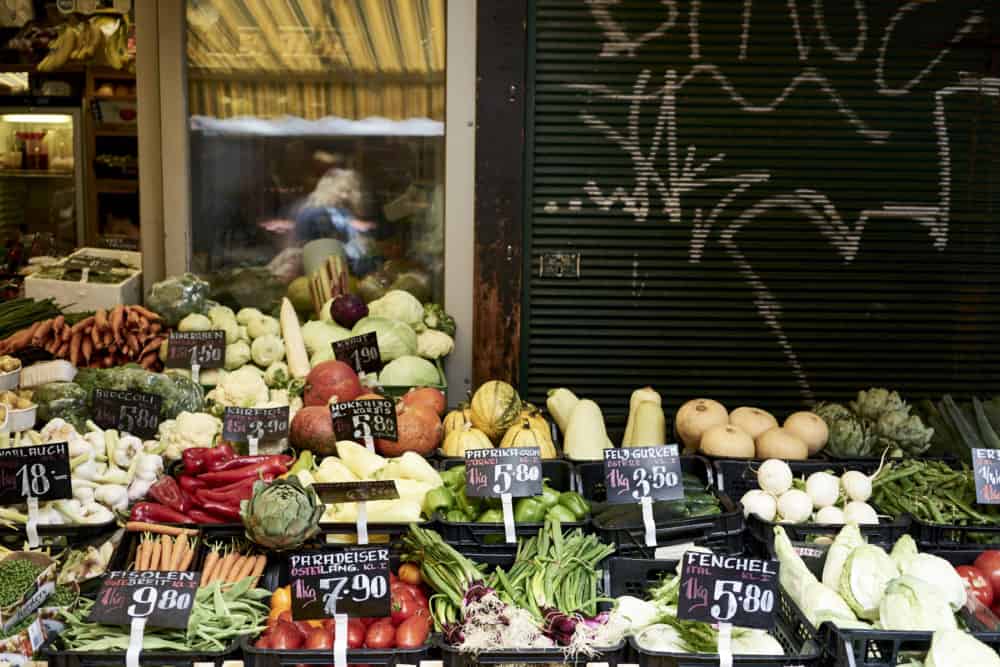 Produce on display at Rochusmarkt, Vienna, including squash, green onions, and tomatoes.