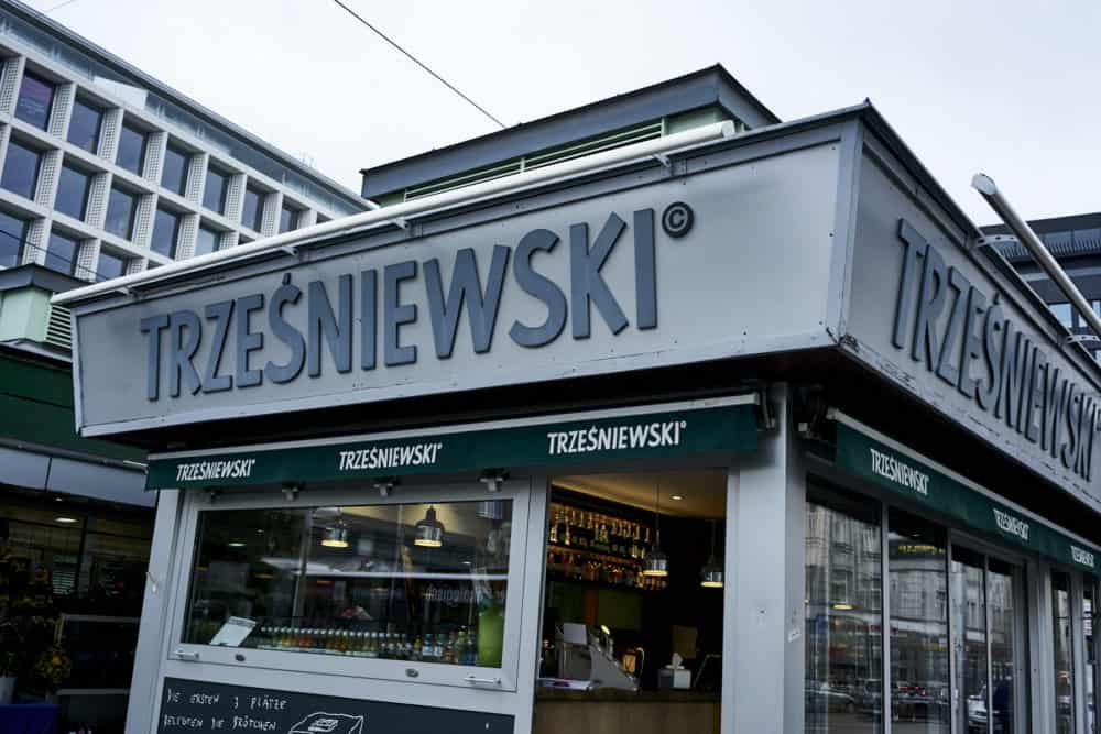 Trzesniewski location at Rochusmarkt Vienna. A small grey building with clear glass walls and green awnings.