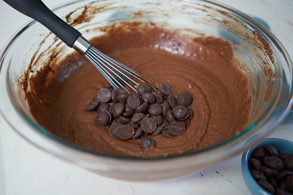A glass bowl with a whisk and brownie batter with chocolate chips. 