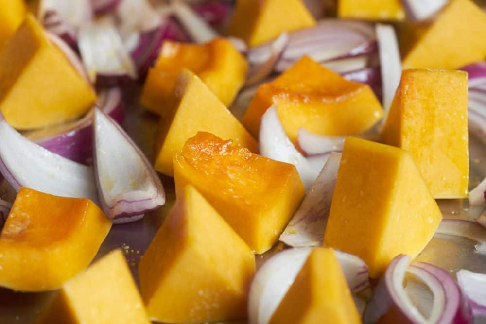 Chopped butternut squash and red onions coated with olive oil on a silver sheet pan. 