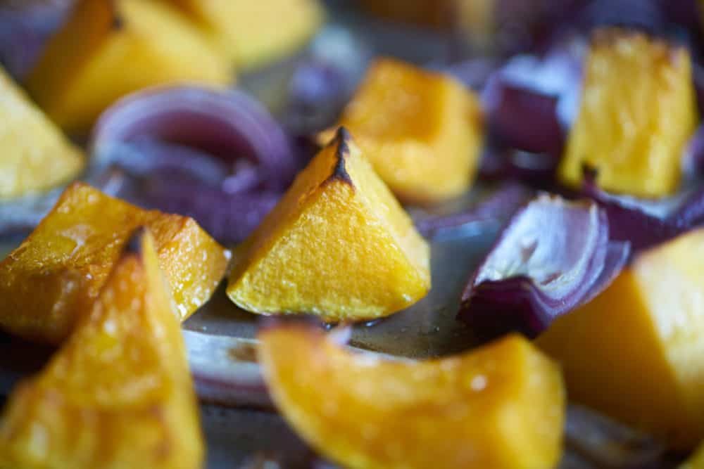 Roasted butternut squash and red onions on a silver sheet pan. 