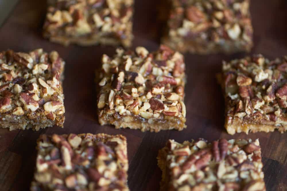 Several square pecan bars on a wooden cutting board. 