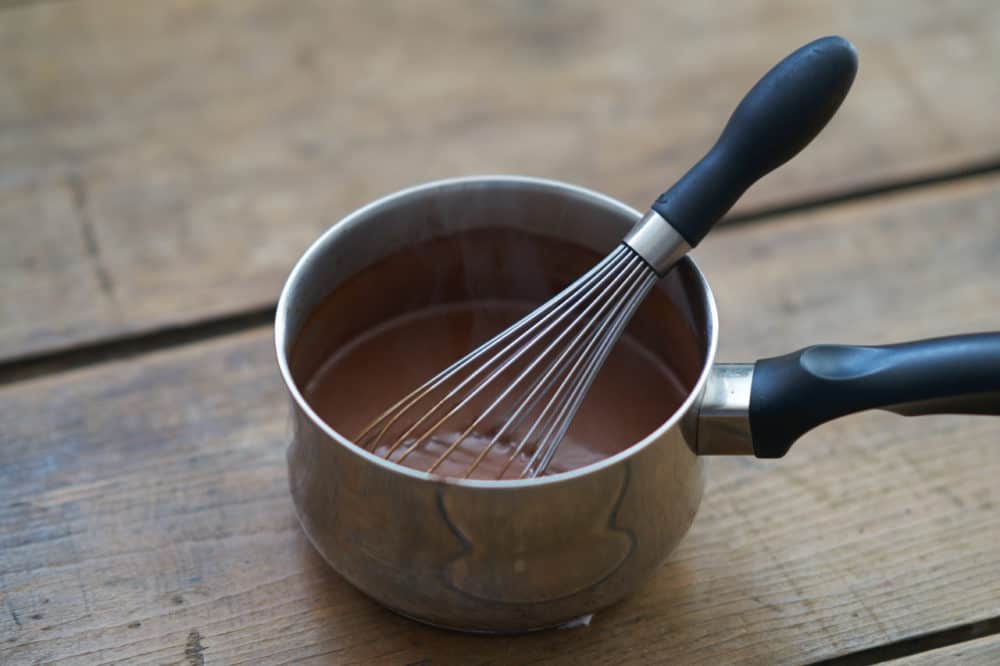A sauce pan filled with French-style hot chocolate with a whisk.