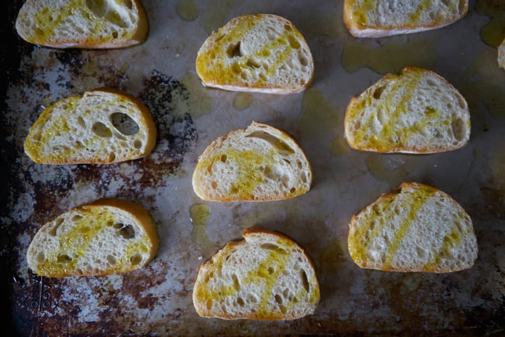 Slices of baguette drizzled with olive oil are arranged on a baking sheet.