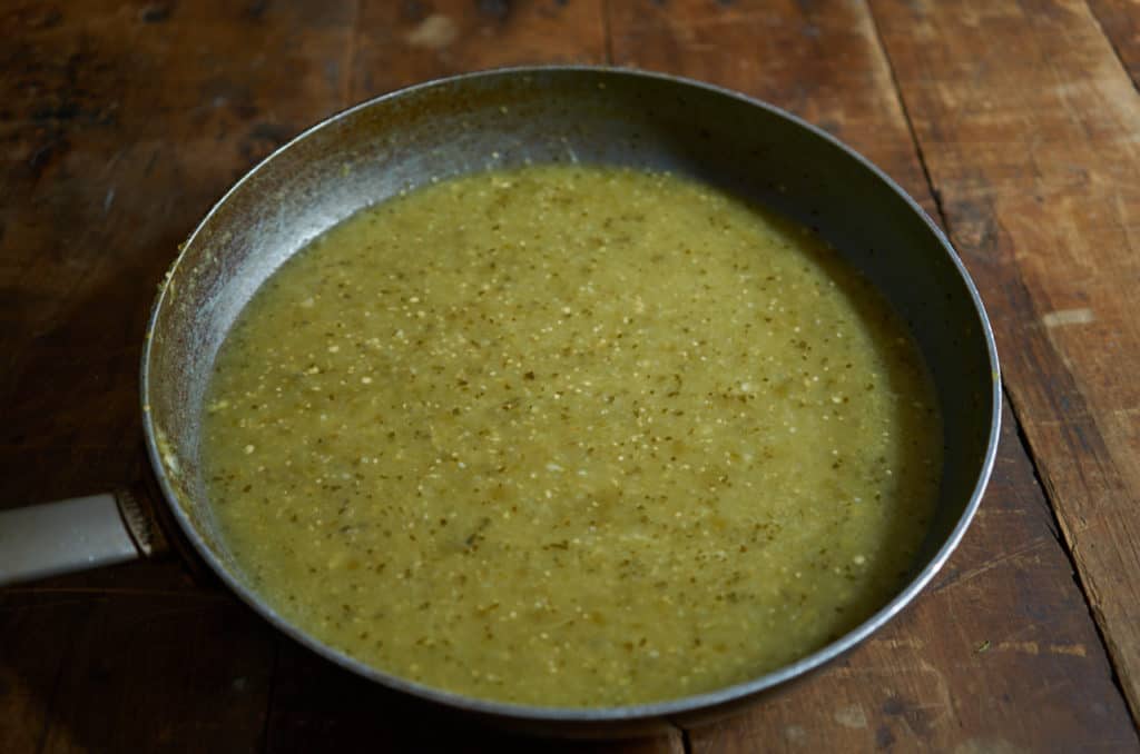 Tomatillo salsa verde that has been cooked down in a skillet on a wooden table top.