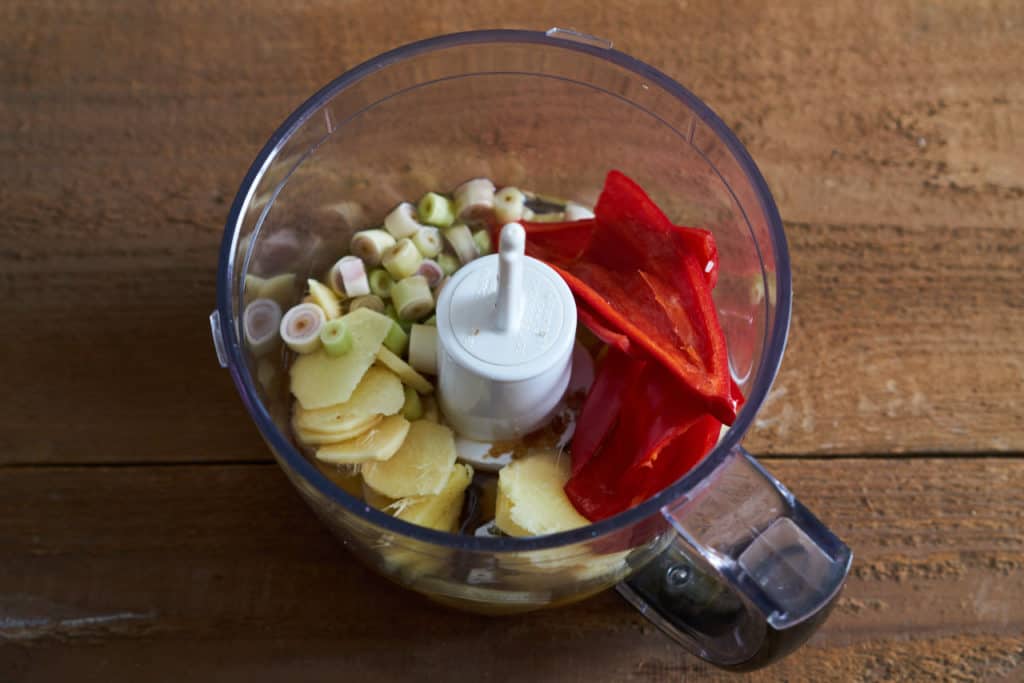 A small food processor containing ginger, lemongrass and chiles, ready to be puréed.