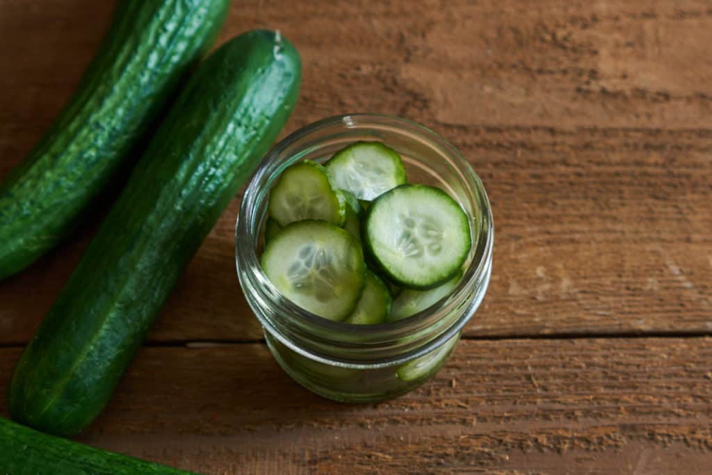 Two small cucumbers sit to the left of a small jar of pickles.