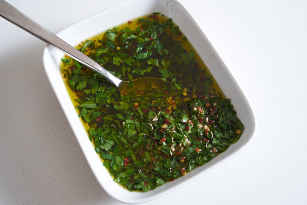 Chimichurri sauce in a white rectangular bowl with a spoon in it.