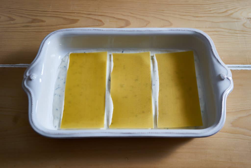 Bechamel sauce and no-boil noodles in a baking dish - the first layer for making butternut squash lasagna.