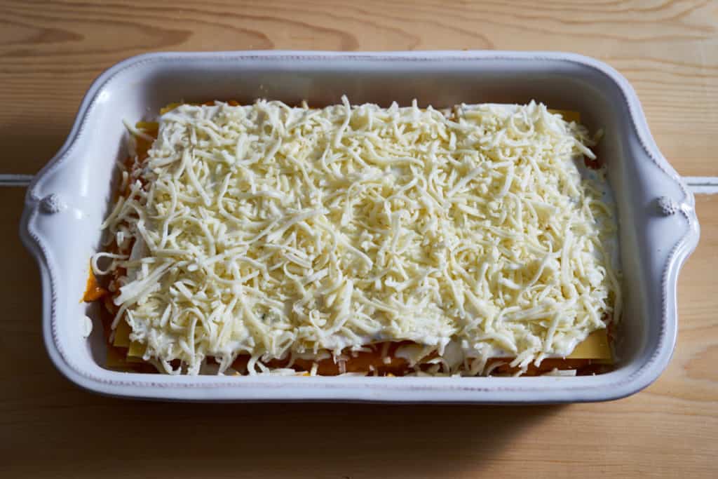 The final layer of cheese is added to butternut squash lasagna prepared in a white baking dish.