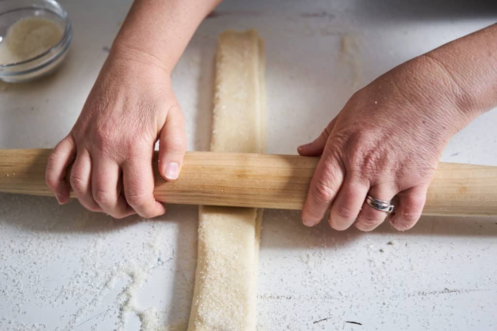 A woman's hands using a rolling pin to put the final crease into palmiers before chilling.