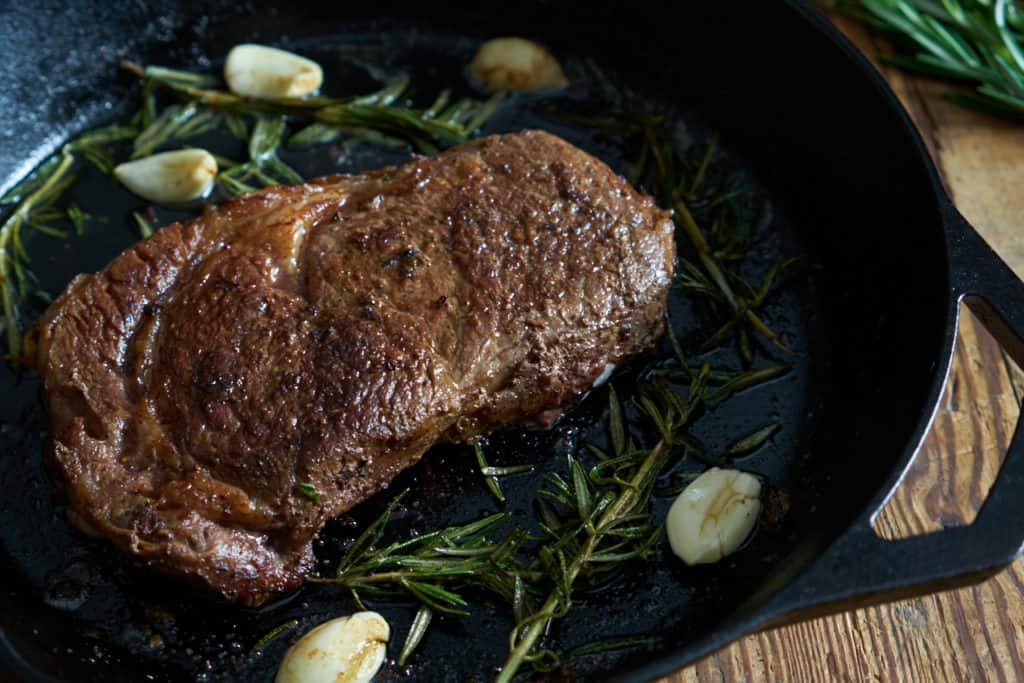 Ribeye steak in a cast iron skillet with rosemary and garlic.