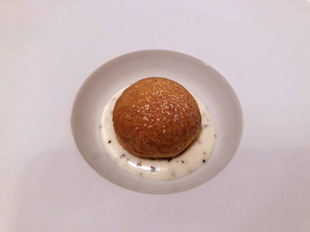 A gougère filled with goat cheese surrounded by a truffle cream in a white dish.