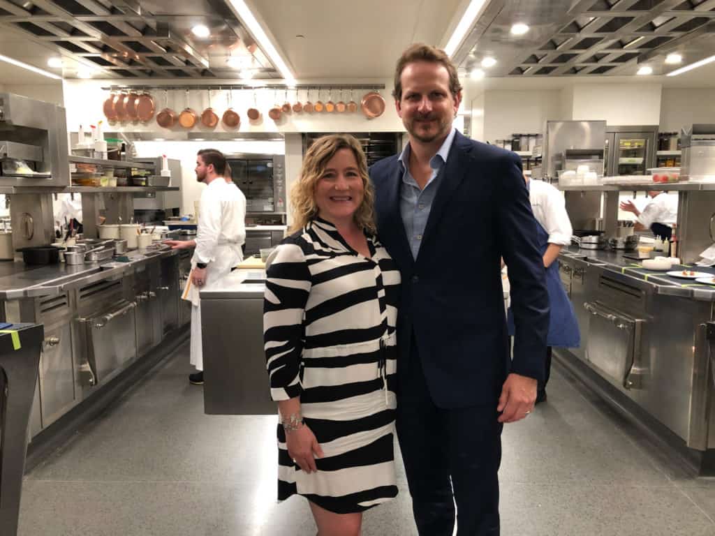 The author and her husband posing for a picture in the kitchen at The French Laundry. She is wearing a black and white dress, he is wearing a blue suit.