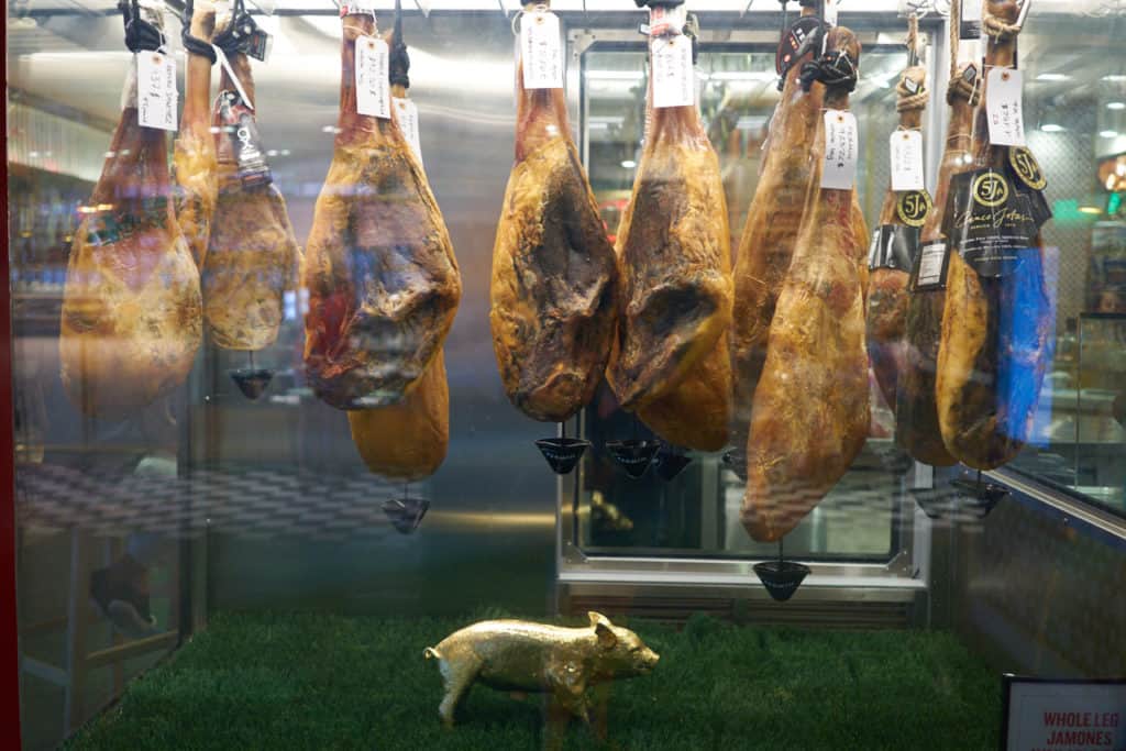 Spanish hams hanging in a case with a decorative gold pig below them.