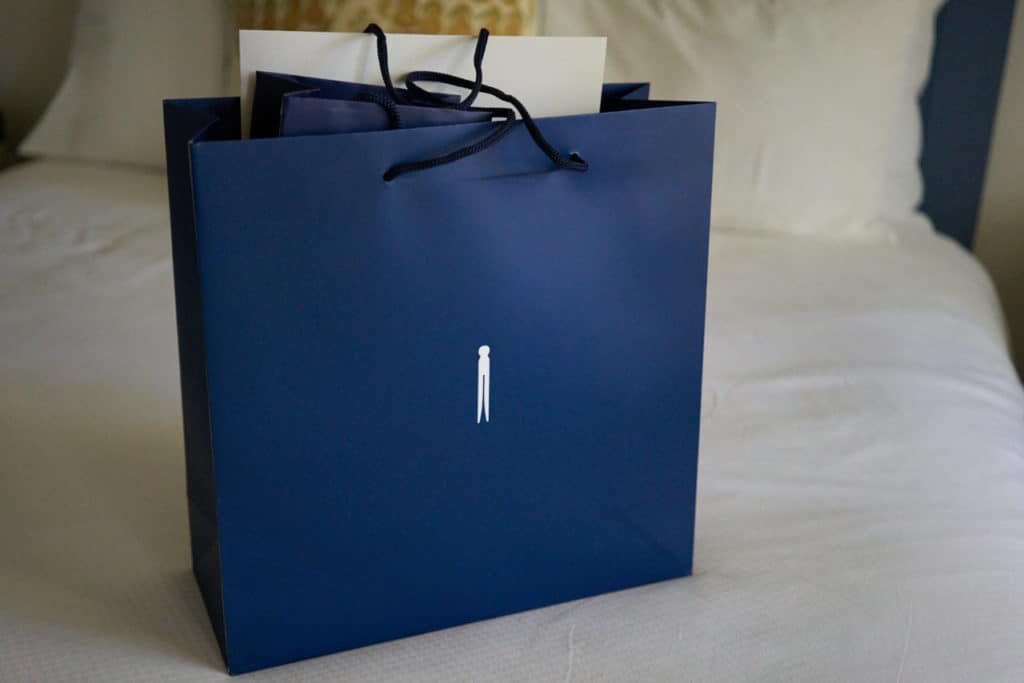 A blue bag with a white clothespin on it sits on a bed.