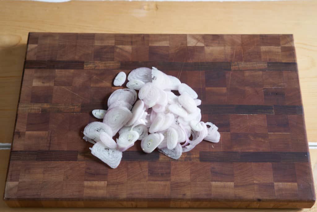 Thinly sliced shallots on a wooden cutting board.