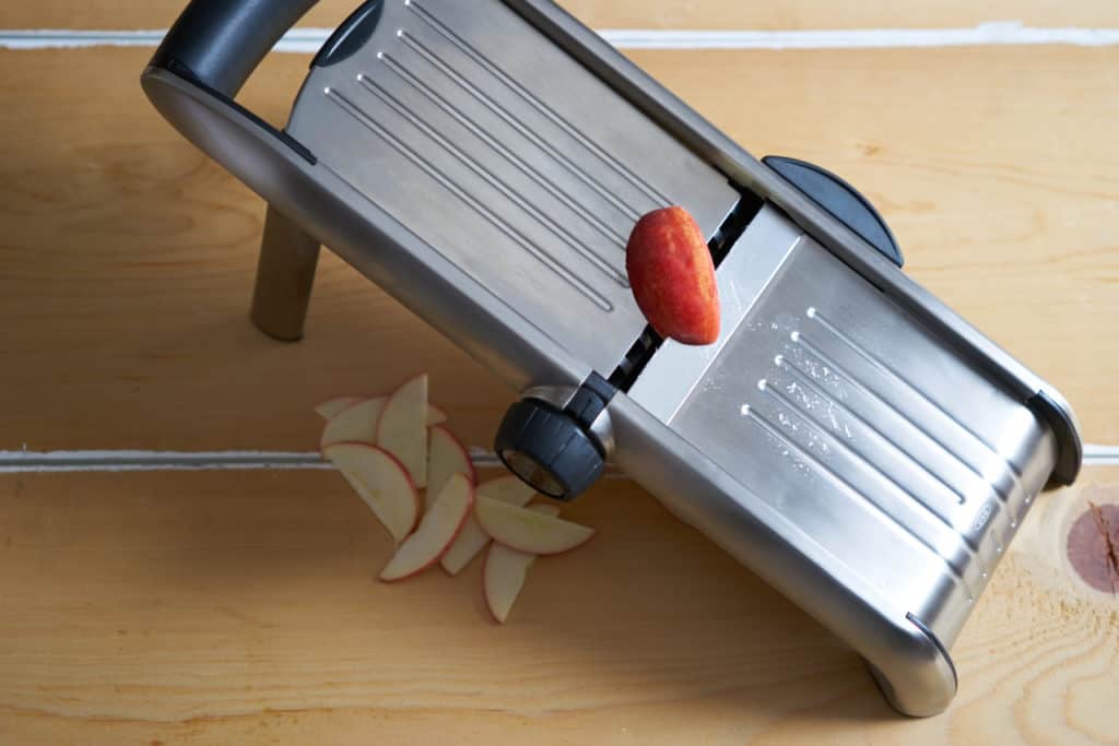 A kitchen mandoline is shown cutting apples.