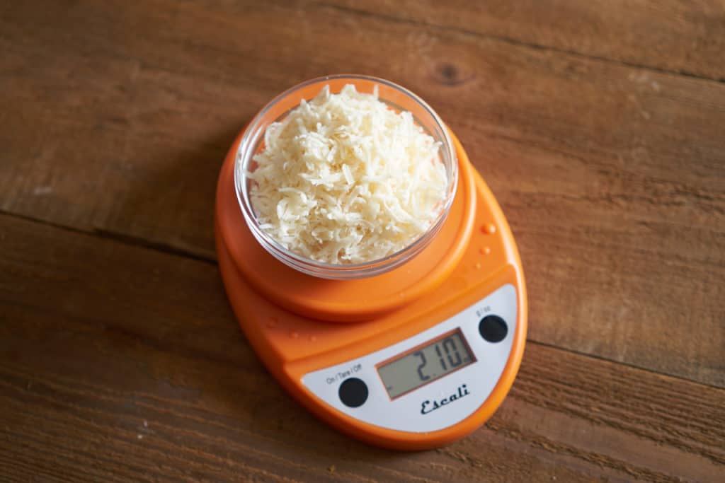 A bowl of grated parmigiano cheese sitting on an orange kitchen scale.