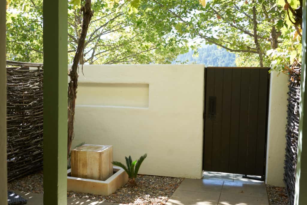 Private patio for one of the Lodge Rooms at Indian Springs, with a stucco wall a water feature, and a wooden gate.