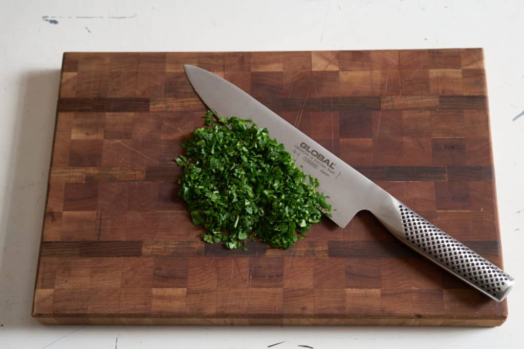A chef's knife and chopped herbs on a wooden cutting board.
