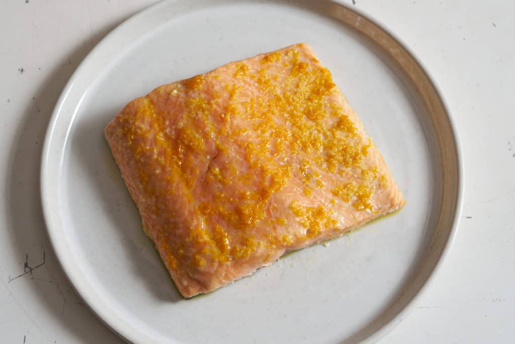 Finished slow roasted salmon with lemon and orange zest on a white plate.