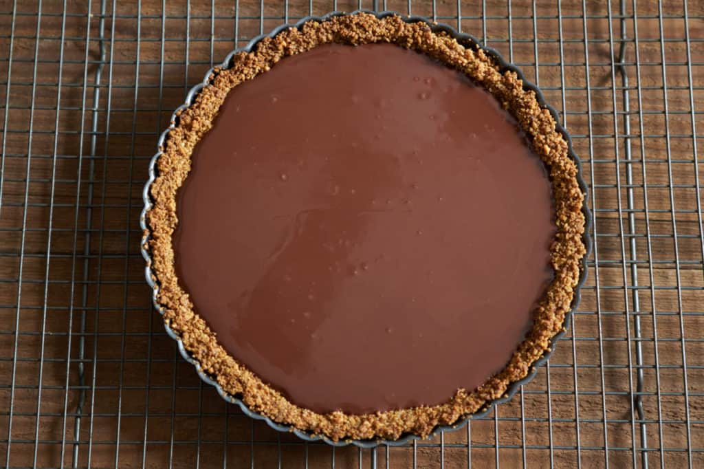Baked gluten free tart crust filled with melted chocolate ready for chilling in the fridge.