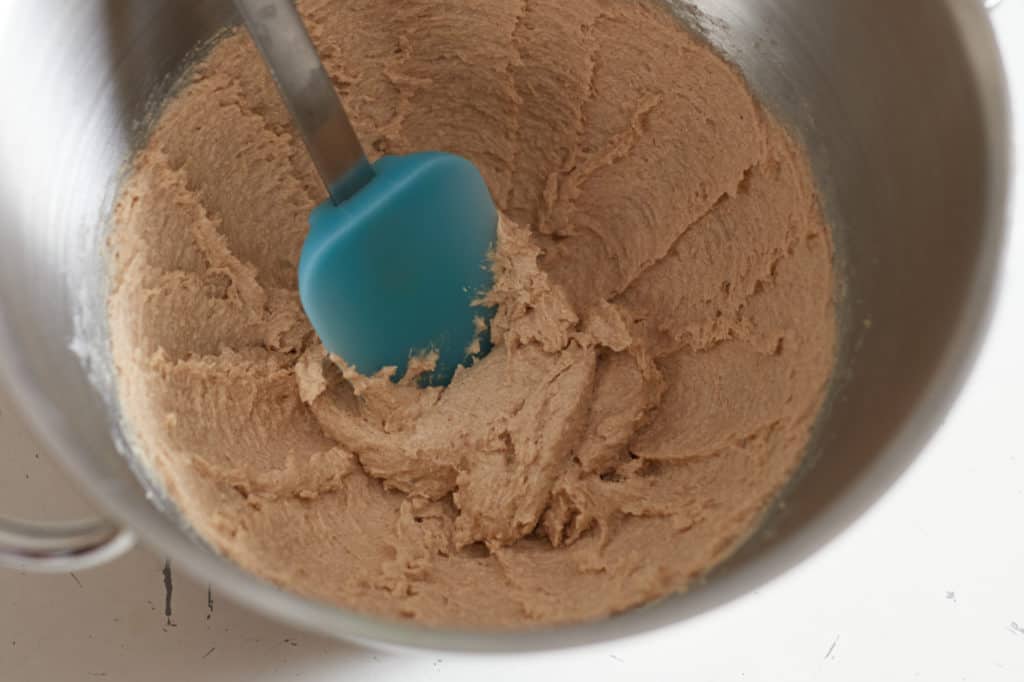 A blue spatula sits in a metal mixing bowl with creamed butter and sugar.