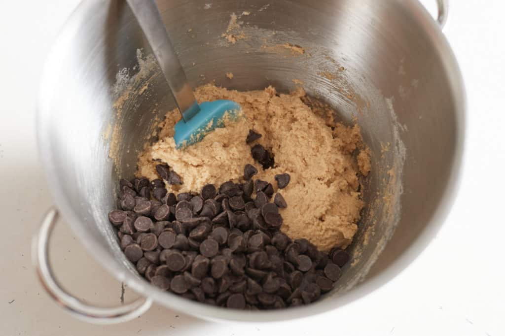 A blue spatula sits in a metal mixing bowl with creamed butter and sugar, and chocolate chips.