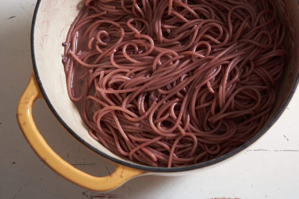 A yellow Dutch oven filled with red wine spaghetti.