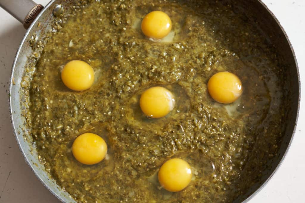 Six raw eggs nestled into the sauce in a large skillet.